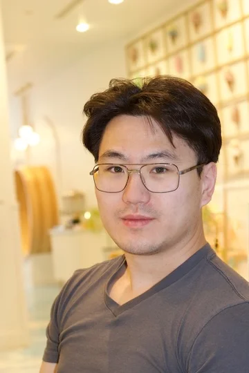 An Asian man in glasses smiles at the camera